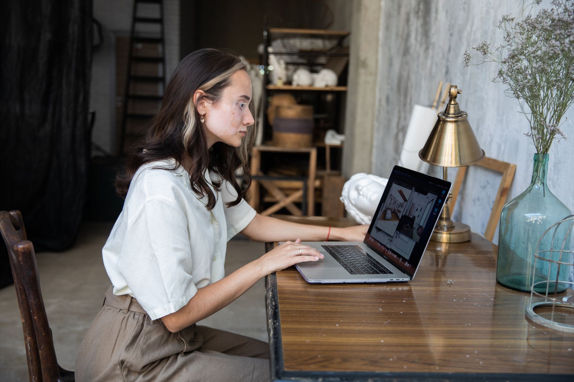 Female artist using a laptop in a stylish art studio with creative decor.