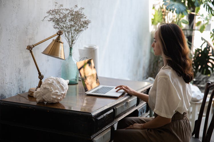 Woman Sitting Behind A Vintage Wooden Desk And Using A Laptop 