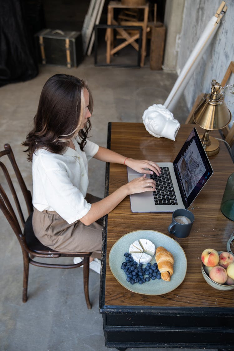 Woman Sitting And Working On A Laptop While Having Lunch 