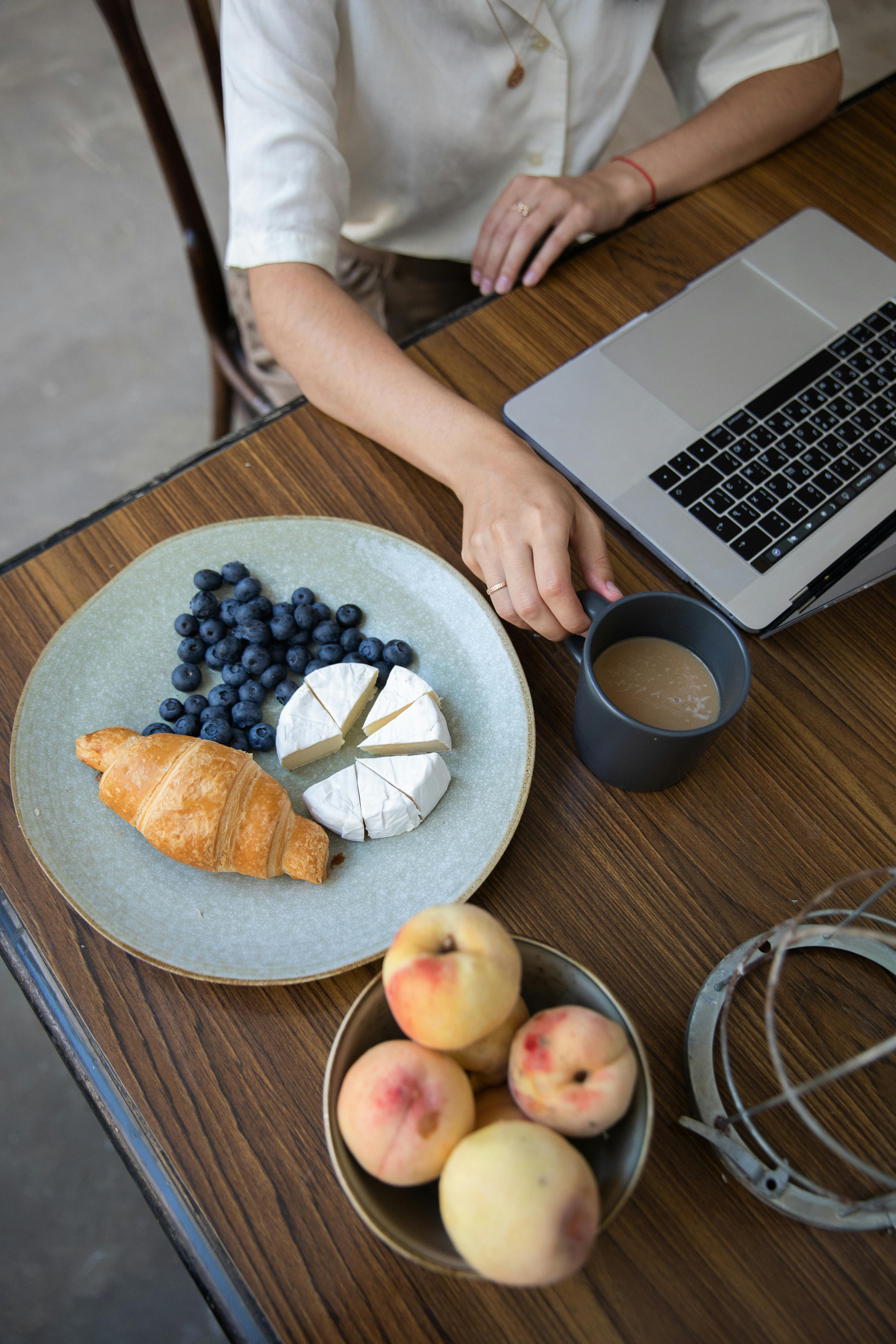 在舒适的室内环境中，咖啡、奶酪和水果与笔记本电脑一同摆放在桌子上