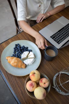 在舒适的室内环境中，咖啡、奶酪和水果与笔记本电脑一同摆放在桌子上