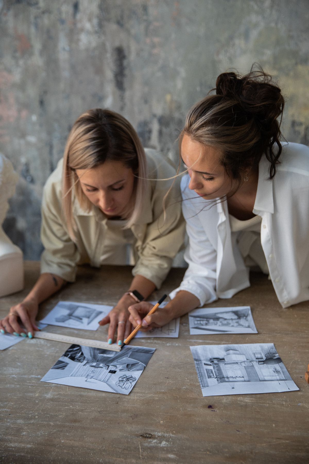 Two women working through a set of prints spread across a wooden table.