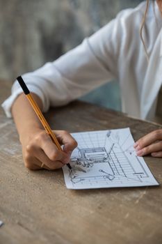 Close-up of a person sketching an interior design on a paper at a wooden table.