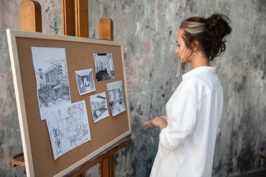Woman in white blouse reviewing interior design sketches on a corkboard.