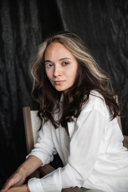 Free Elegant portrait of a woman seated with a relaxed expression against a dark background. Stock Photo