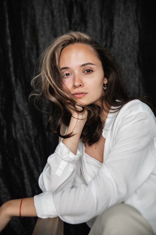 Free Portrait of a woman in a white shirt posing with a thoughtful expression against a dark backdrop. Stock Photo
