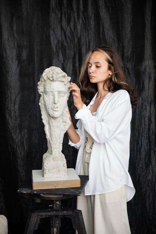 Woman in White Long Sleeve Dress Holding White Animal Statue