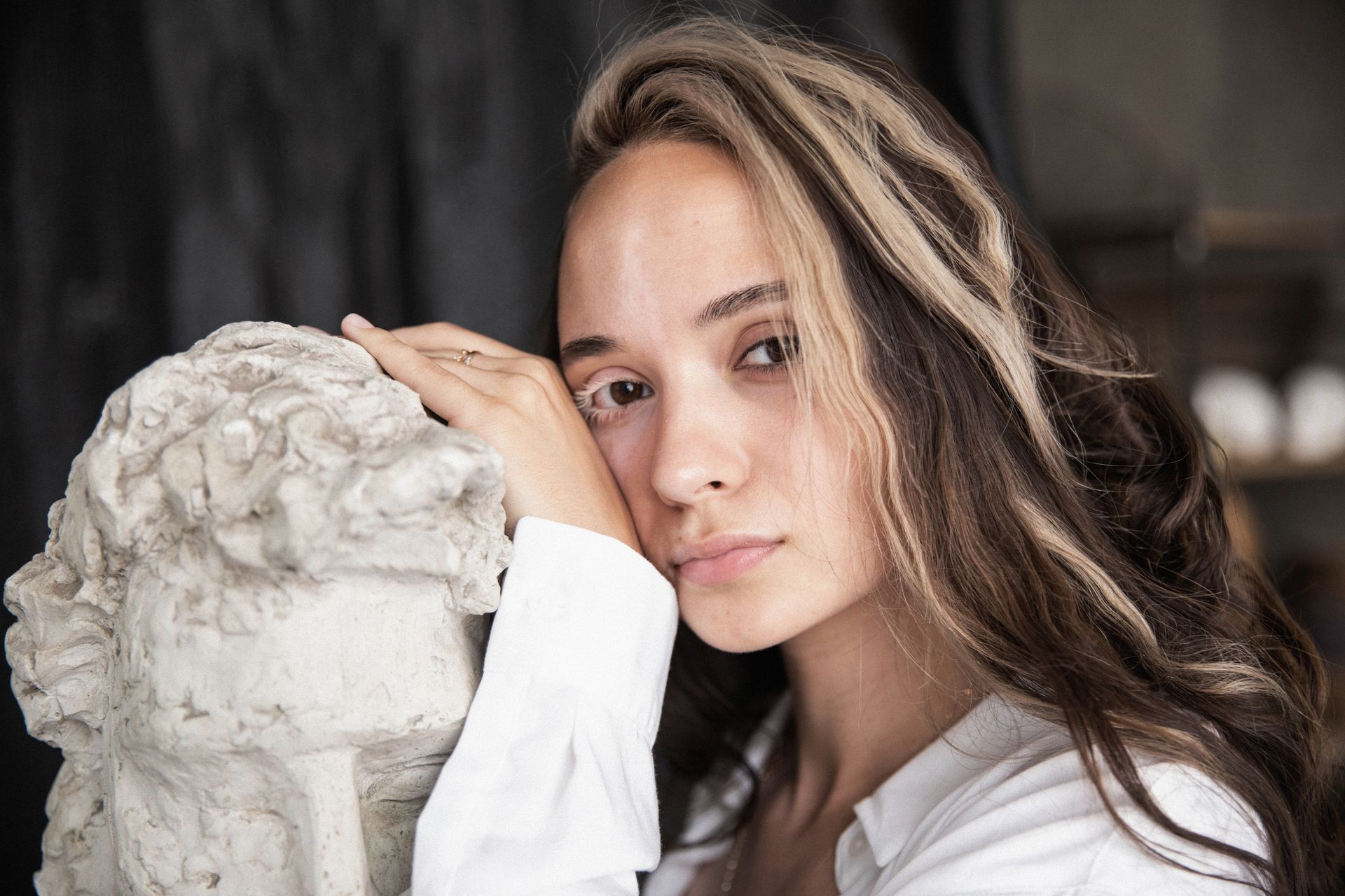 A woman poses thoughtfully beside a plaster sculpture. Artistic and serene setting.