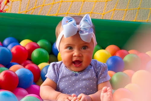 Cute Baby in Blue and White Polka Dot Shirt Surrounded by Plastic Balls