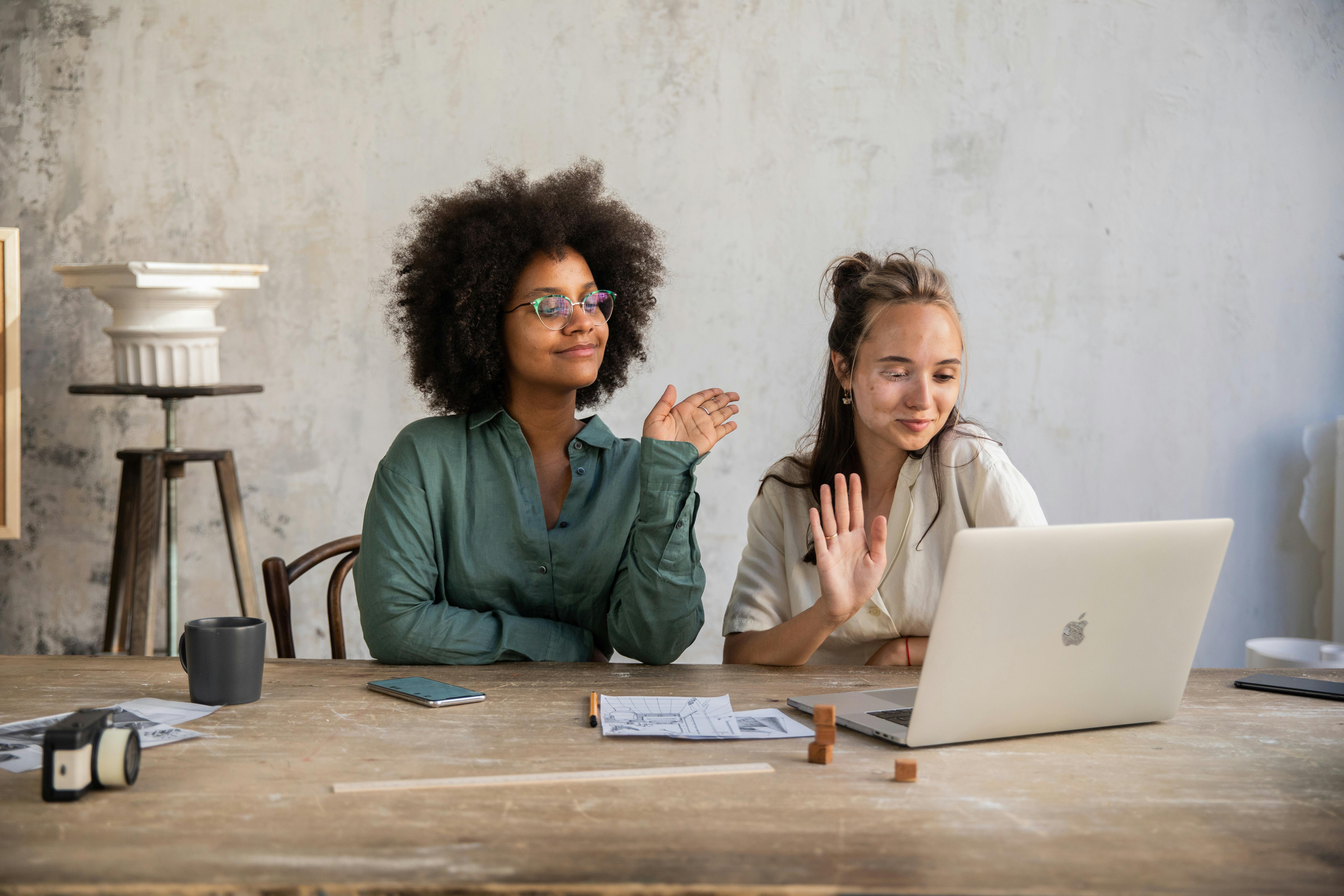 two women having their hands while looking at a laptop