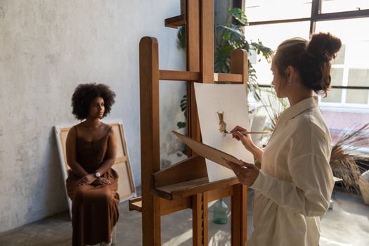 A diverse artist painting a model in a sunlit studio, showcasing creativity and diversity.
