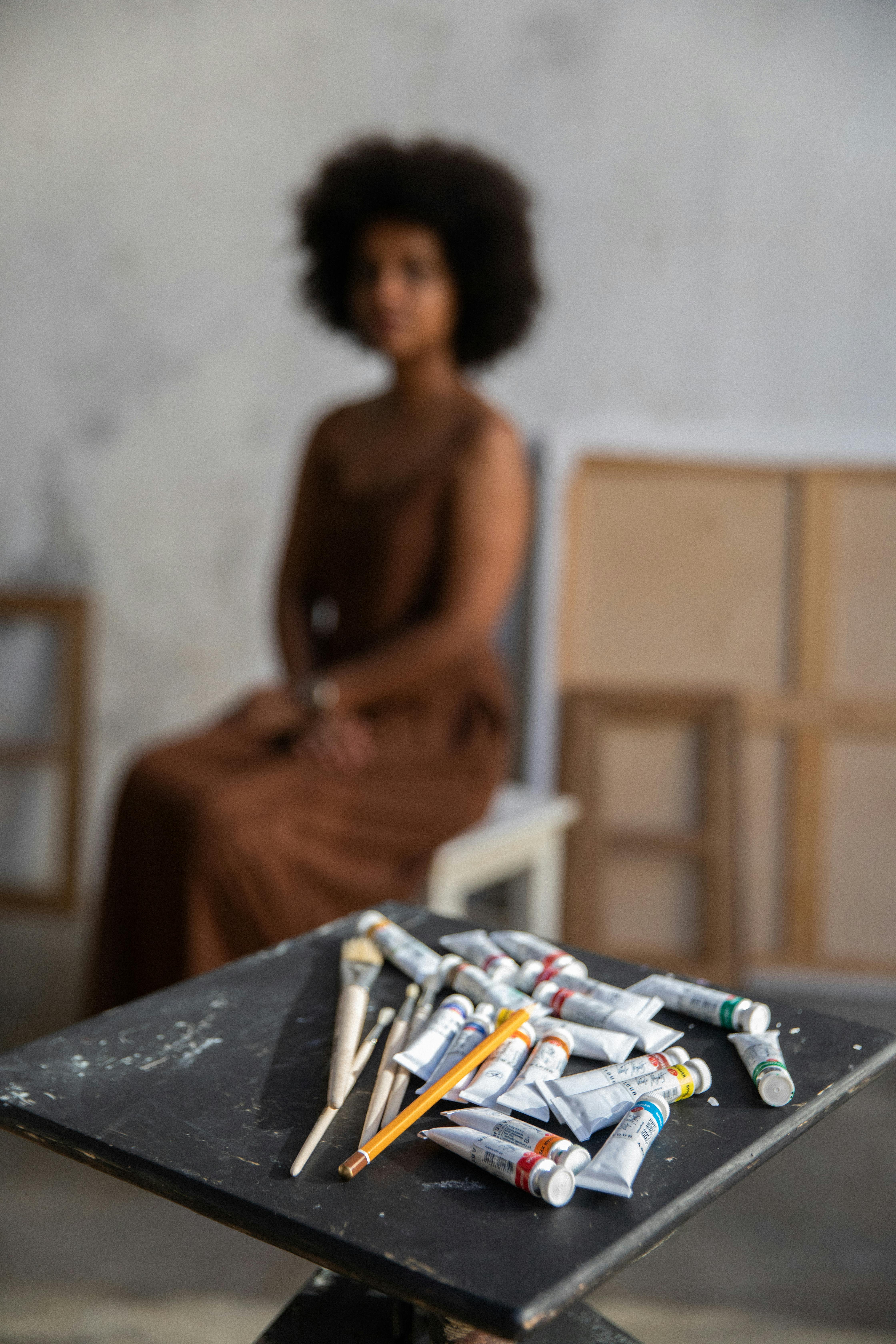 A creative workspace featuring acrylic paints and an artist in a blurred background.
