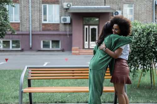 Free Two friends embrace warmly outside near a building on a sunny day, showcasing friendship and happiness. Stock Photo