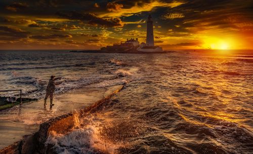 Free A fisherman casts a line during a golden sunset by St Mary's Lighthouse in Whitley Bay, UK. Stock Photo
