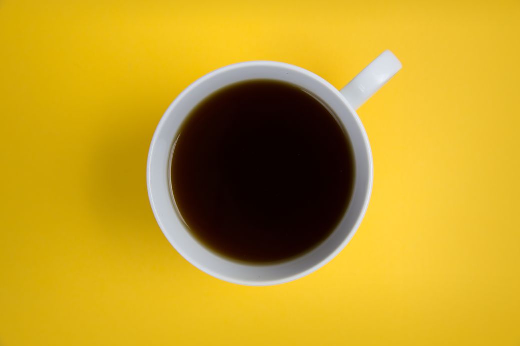 A white cup of black coffee seen from above on a yellow surface — photo by Foodie Factor on Pexels