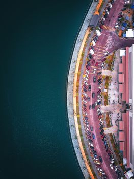 Aerial top view of contemporary city waterfront with curvy road and parking lots located near tranquil rippling sea on clear summer weather