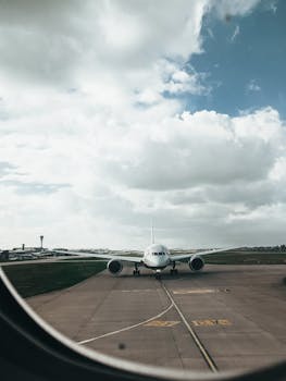 A view through an airplane window capturing a commercial airliner taxiing on a runway in daylight.