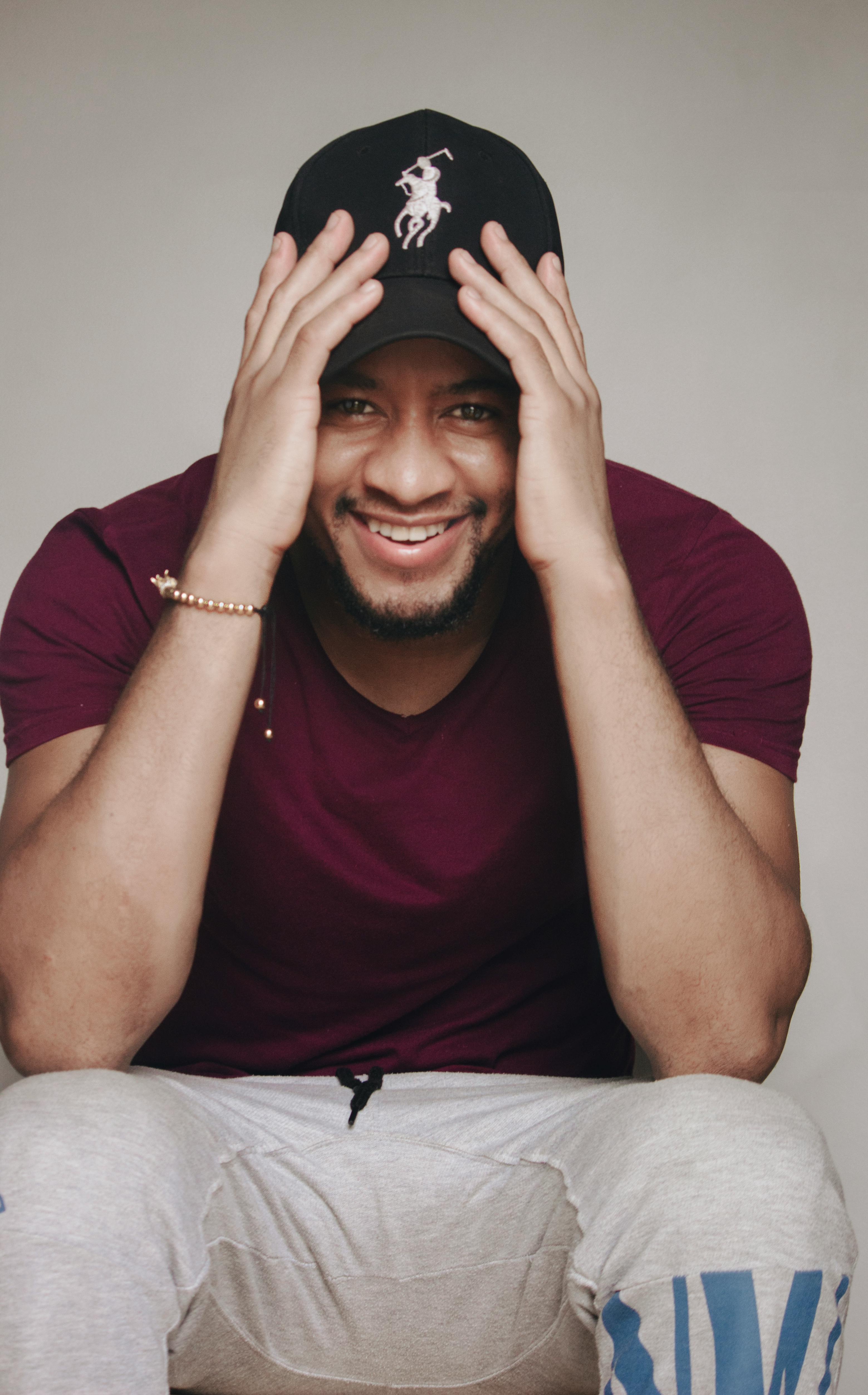 Cheerful man wearing a maroon shirt and black cap smiles in a studio portrait.