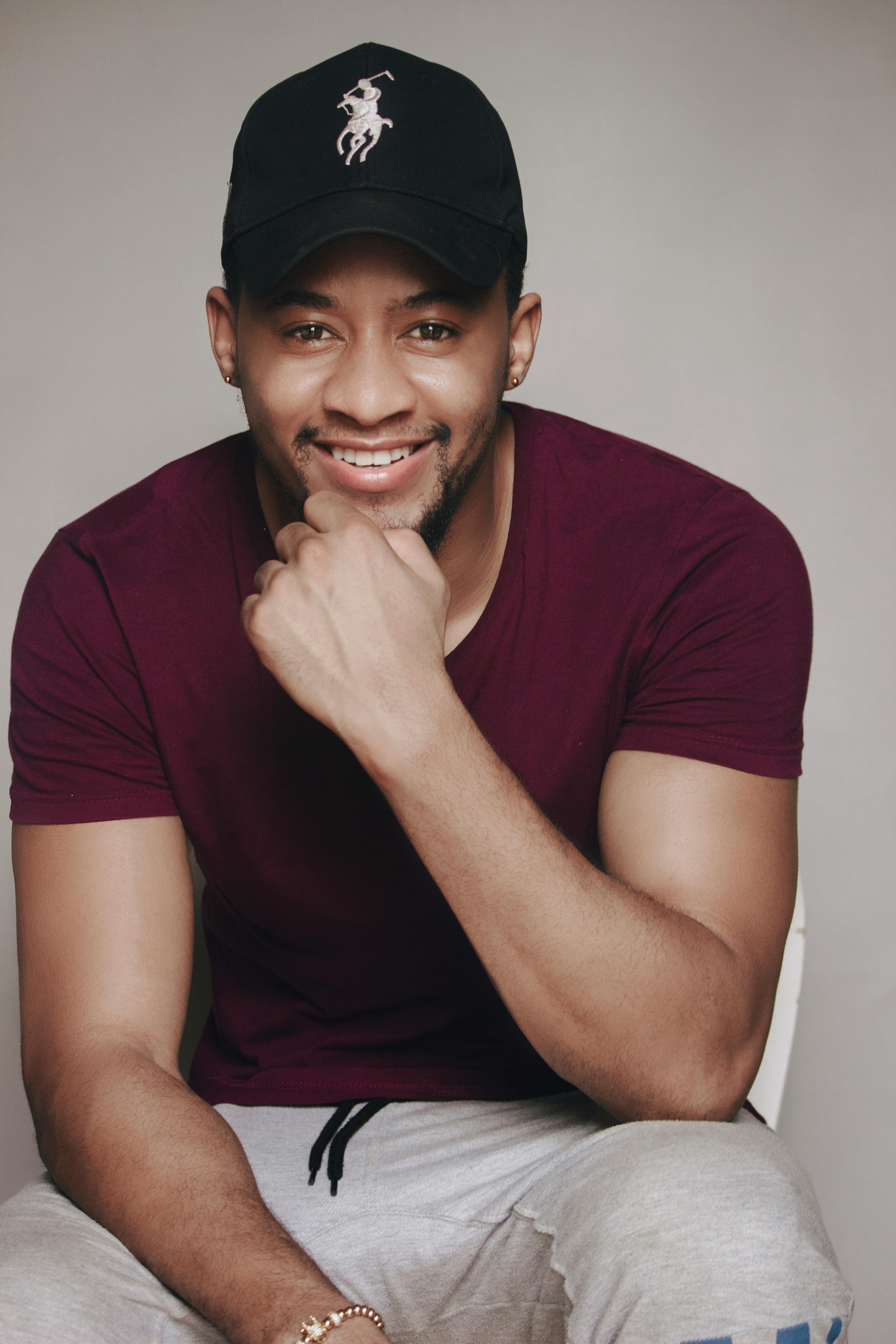Studio portrait of a cheerful man wearing a maroon shirt and black cap, smiling at the camera.
