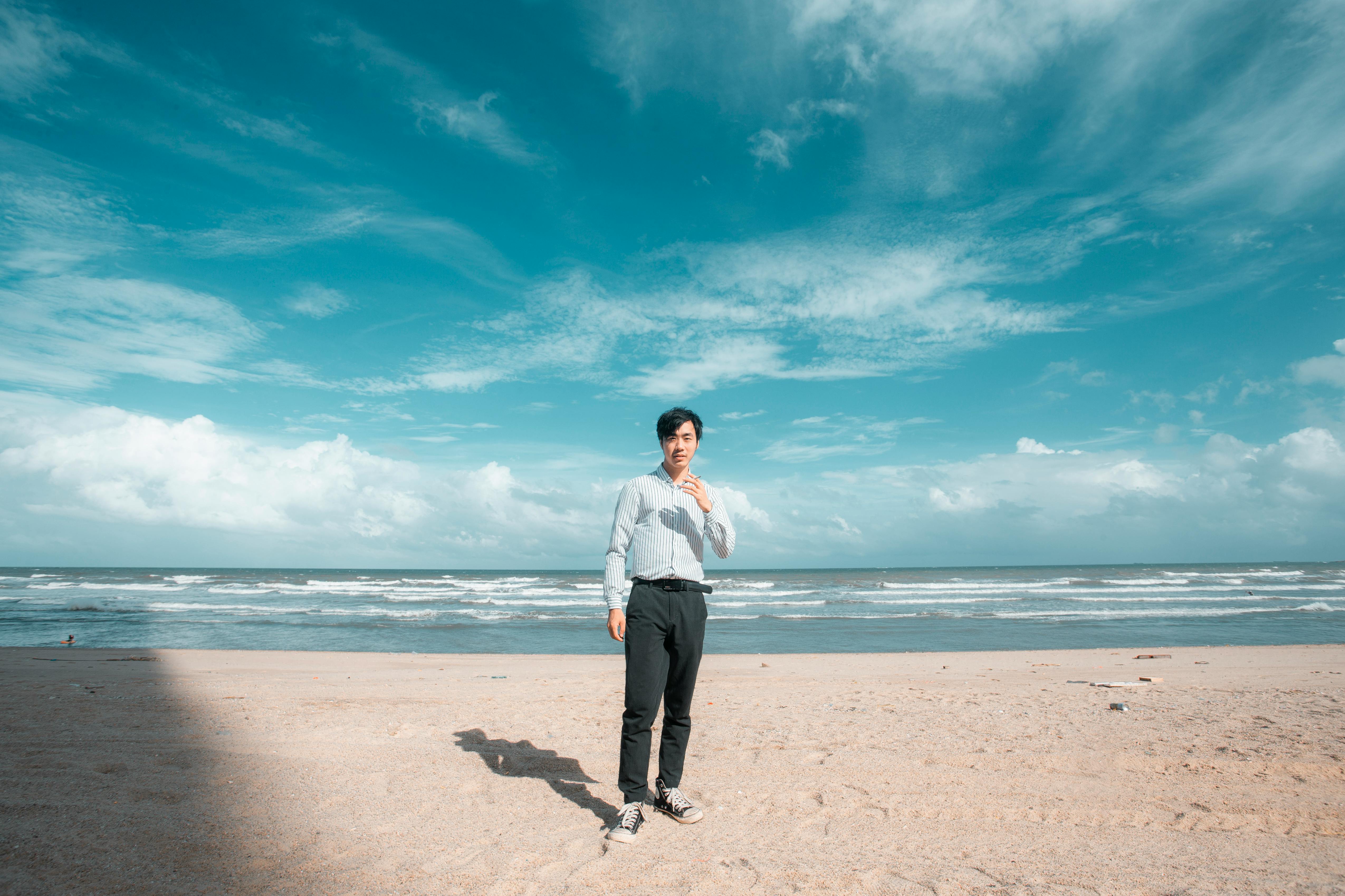 阳光明媚的海滩上，一个穿着正装衬衫的年轻人站在蓝天下