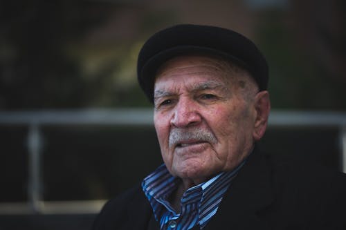 Free Contemplative elderly male with mustache in trendy apparel and cap looking at camera near fence Stock Photo