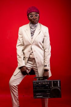 Man in white suit holding a vintage radio against a bold red background.