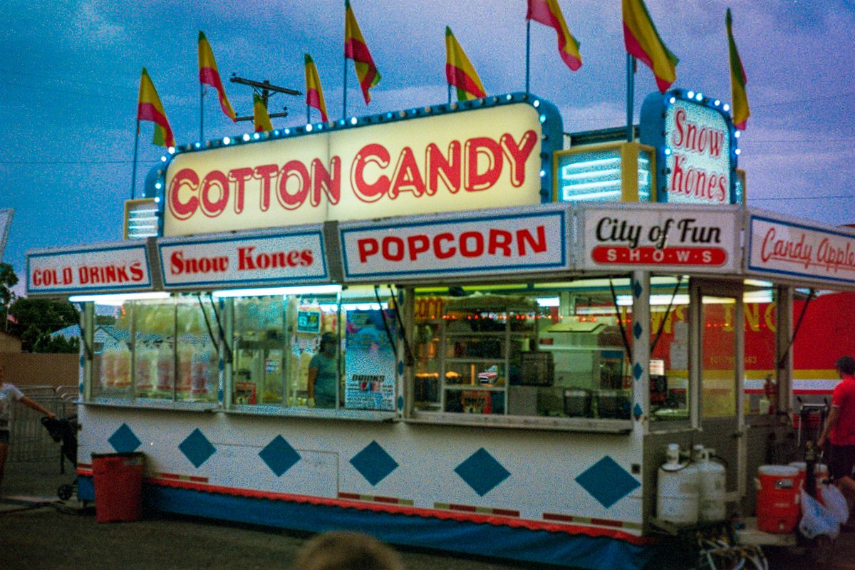 Cheerful candy booth at a funfair offering cotton candy and more, captured at twilight.