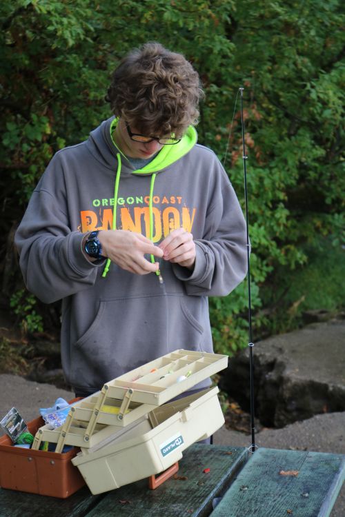 Free Teenager prepares fishing lure in Oregon outdoor park with green foliage. Stock Photo