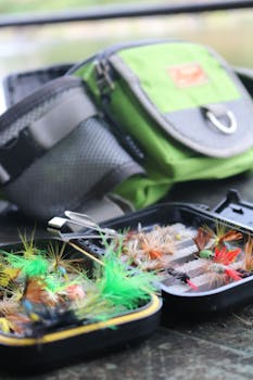 Close-up of colorful fishing lures in a tackle box with green bag outdoors.