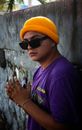 Photo of a Man in a Yellow Hat and Purple T-Shirt standing by a Wall