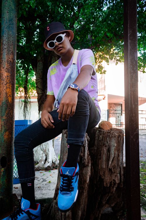 Free Stylish young man with sunglasses and bucket hat posing on a log outdoors in Mexico. Stock Photo