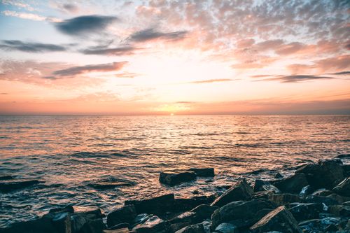 Free Spectacular view of coast with stones against rippled ocean under shiny cloudy sky at sundown Stock Photo
