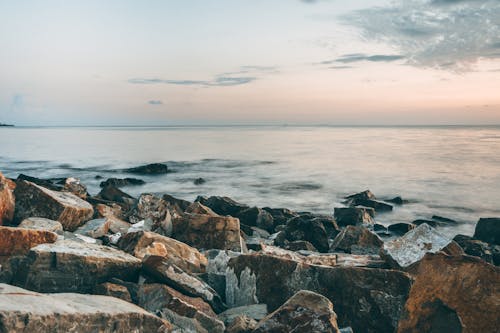 Scenic view of rocky formations on coast against rippled sea with horizon under cloudy sky at sunset