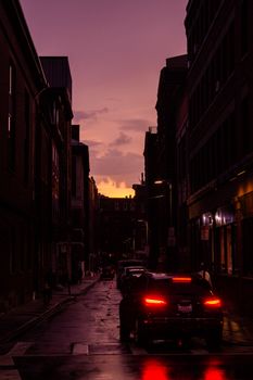 Silhouetted buildings line a Boston street at dusk, with warm sunset hues enhancing the scene.