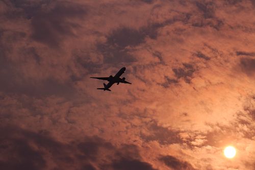 Free Silhouette of an airplane flying against a vibrant sunset sky with scattered clouds. Stock Photo