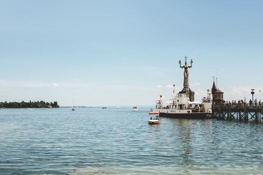 A picturesque view of Konstanz harbor featuring the Imperia statue and serene waters under a clear blue sky.
