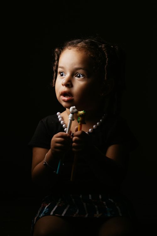Free Adorable black haired kid with dark eyes in casual clothes holding plastic toy and looking away with open mouth Stock Photo