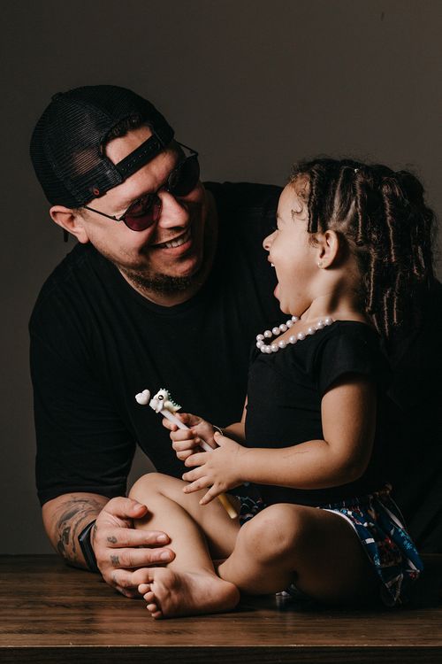 Free Brutal tattooed man in cap and glasses looking at charming little daughter in casual clothes and smiling Stock Photo