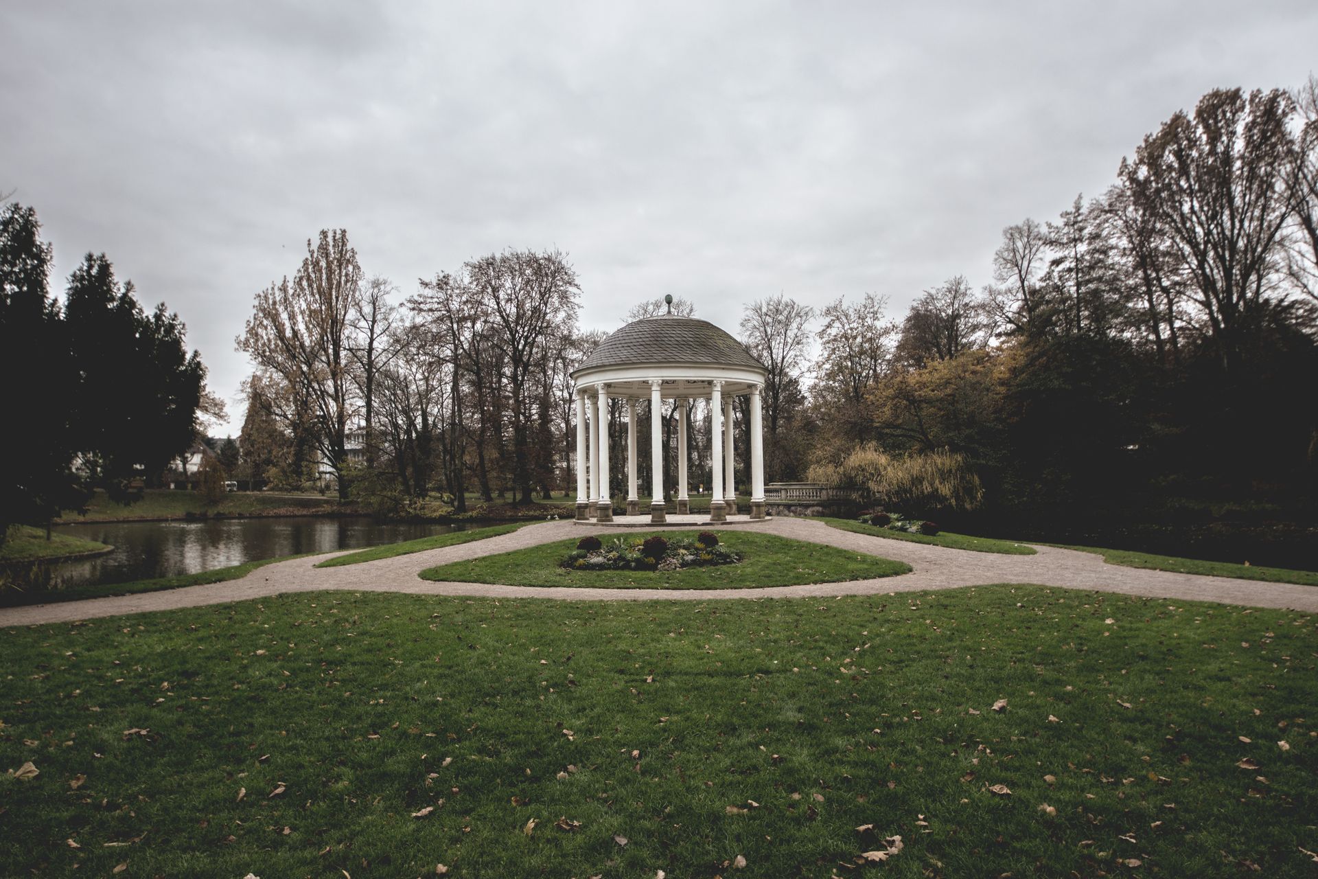 A serene pavilion set amidst lush lawns and trees in Strasbourg's botanical gardens under a cloudy sky.