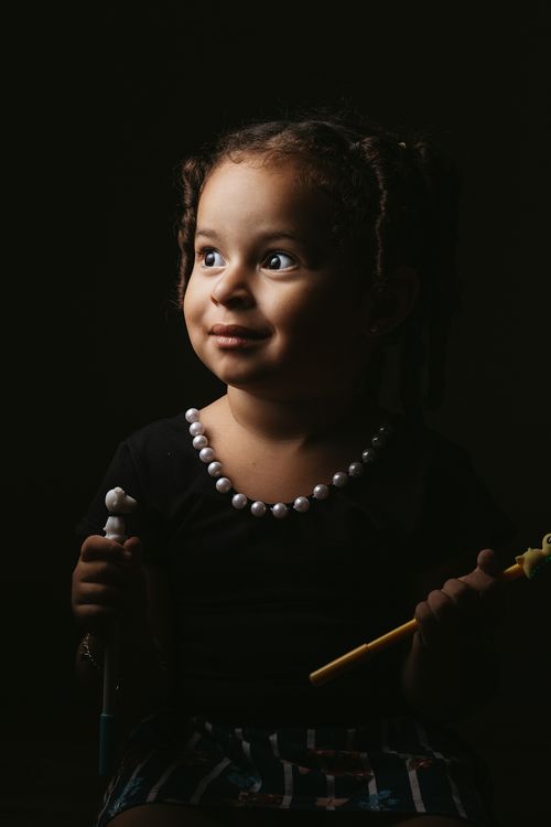 Free Charming kid with braids in casual clothes sitting in studio with pen in hands and looking away Stock Photo