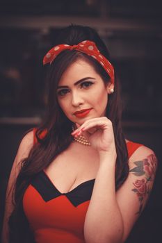 Elegant woman in vintage style with rose tattoo and red polka dot headband, striking a confident pose.