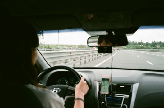 Crop anonymous female holding steering wheel and driving car along asphalt roadway in daytime