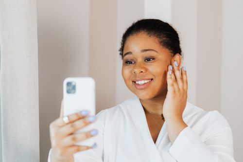 Free A joyful woman in a white top smiles while taking a selfie indoors. Stock Photo