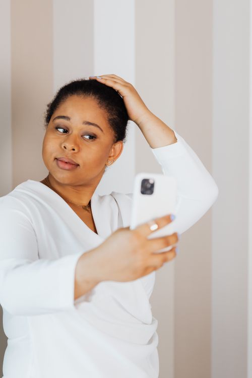 Free A woman in a white top taking a selfie, posing indoors with a smartphone. Stock Photo