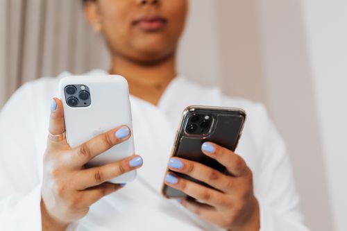 Free Close-up of a person with blue nails holding two smartphones indoors. Stock Photo