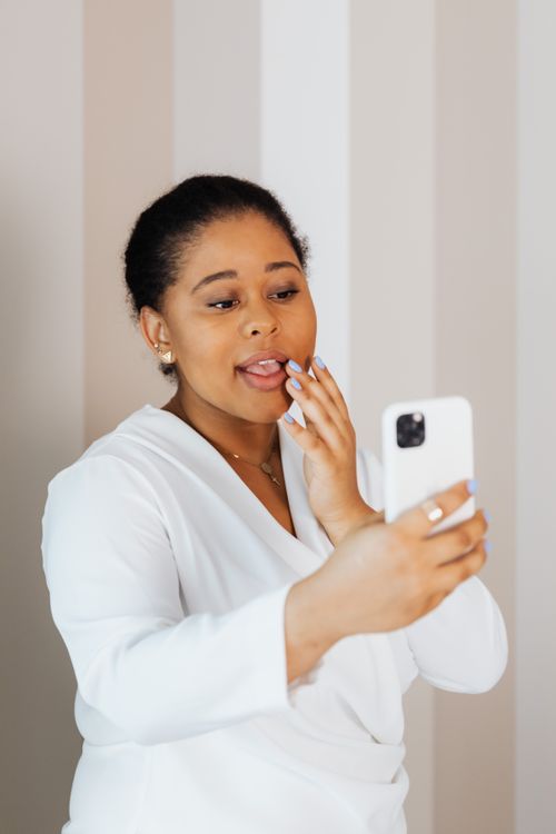 Free African American woman taking a selfie indoors, using a smartphone, wearing a white top. Stock Photo