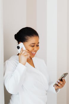 Happy woman in white top using smartphone indoors for a call.