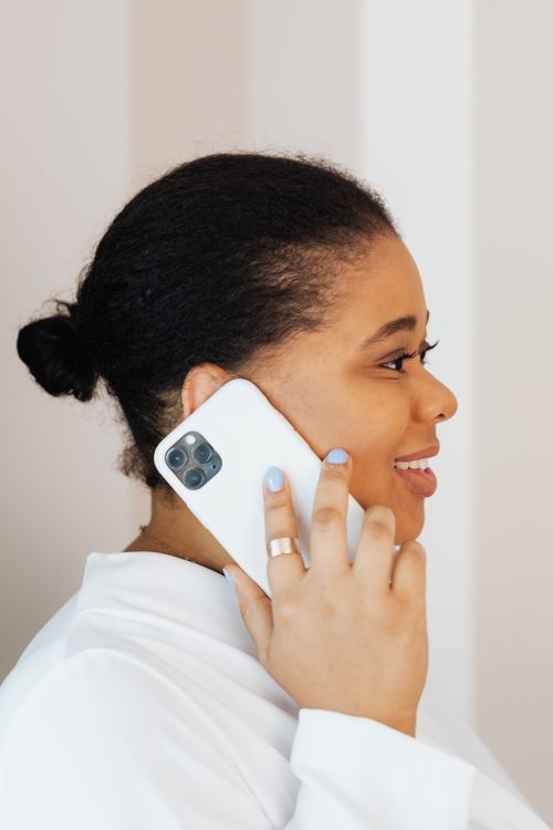 Free Side profile of a smiling woman in a white top talking on a smartphone indoors. Stock Photo
