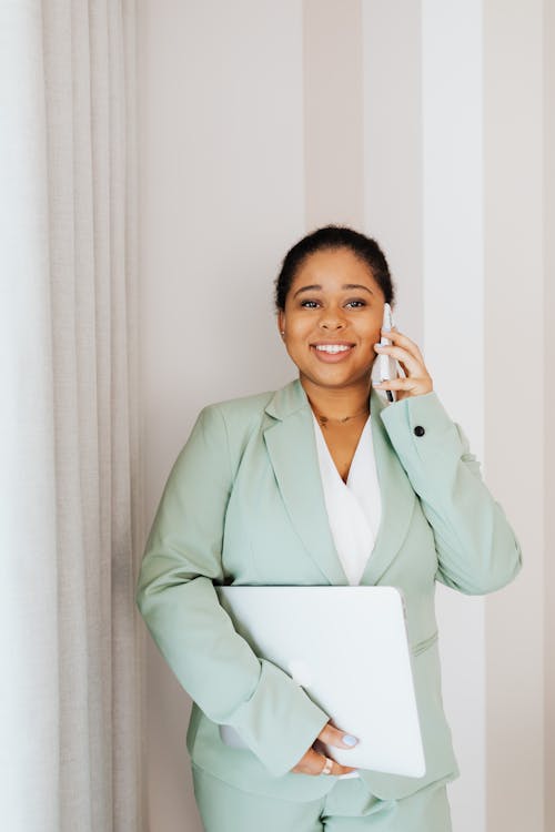 Free Woman in Light Green Suit Standing while Talking on Cellphone Stock Photo