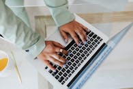 特写镜头：一个女人在柔和的灯光下，用涂着淡蓝色指甲油的手指在笔记本电脑上打字